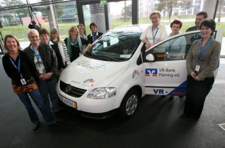 A diverse group of individuals gathered beside a white van, engaged in conversation and enjoying each other's company.  