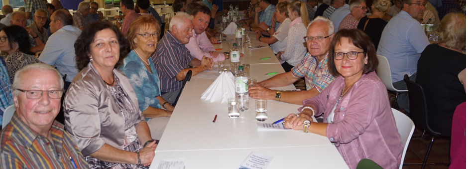 Eine Gruppe von Menschen sitzt drinnen an einem Tisch, lächelt sich an und genießt die Gesellschaft der anderen.
