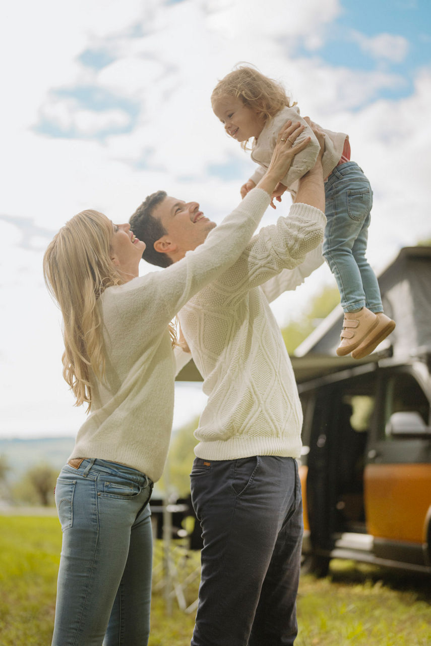 Junges, glückliches Ehepaar hält Kind in die Luft.