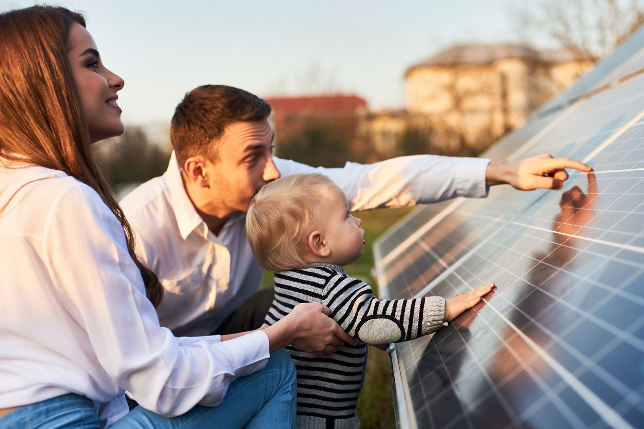 Seitliche Nahaufnahme: Eine junge Familie mit ihrem kleinen Sohn erkundet an einem sonnigen Tag eine Solaranlage