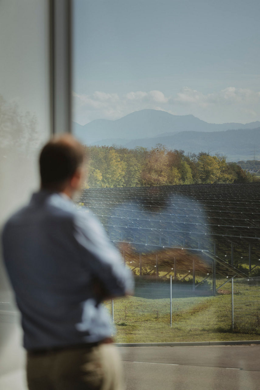 Mann schaut aus dem Fenster auf ein Solarfeld - im Hintergrund der Belchen.