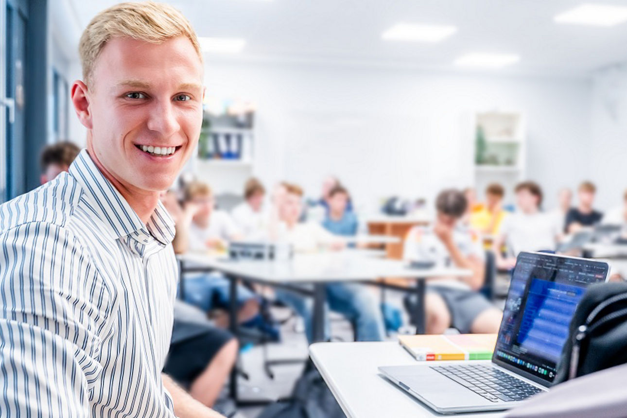 Person schaut in die Kamera, die Klasse sitzt im Hintergrund