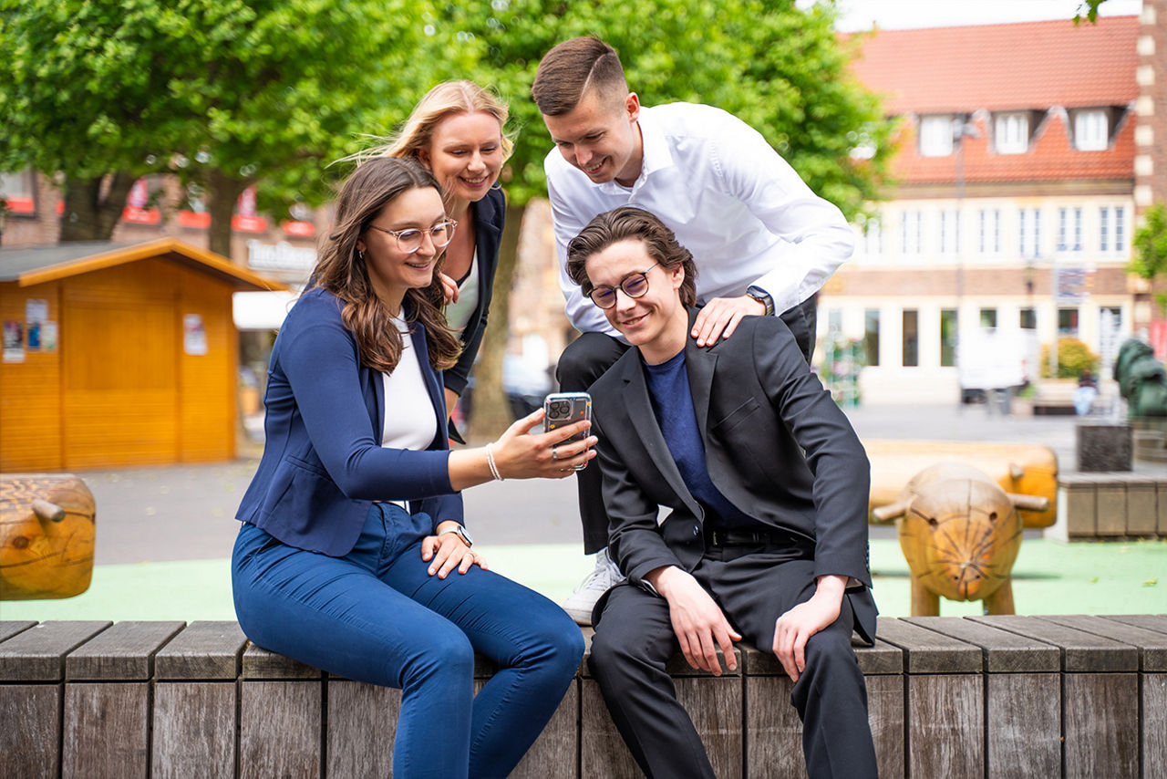 4 Personen sind draußen und schauen auf ein Handy