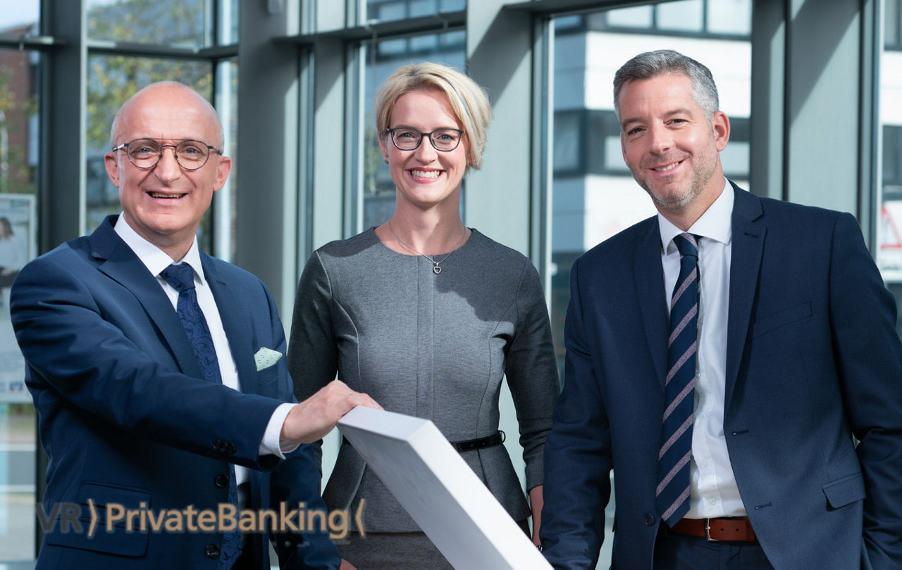 Drei Mitarbeiter des VR PrivateBanking schauen in die Kamera