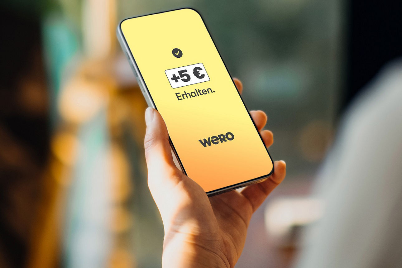 Person hält ein Handy und bekommt die Meldung 5€ durch die erstmalige nutzung von Wero erhalten zu haben