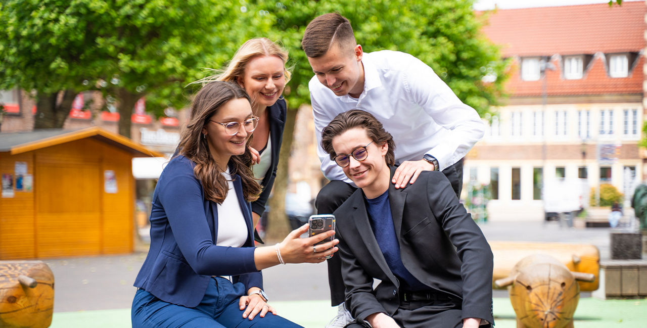 4 Personen sind draußen und schauen auf ein Handy