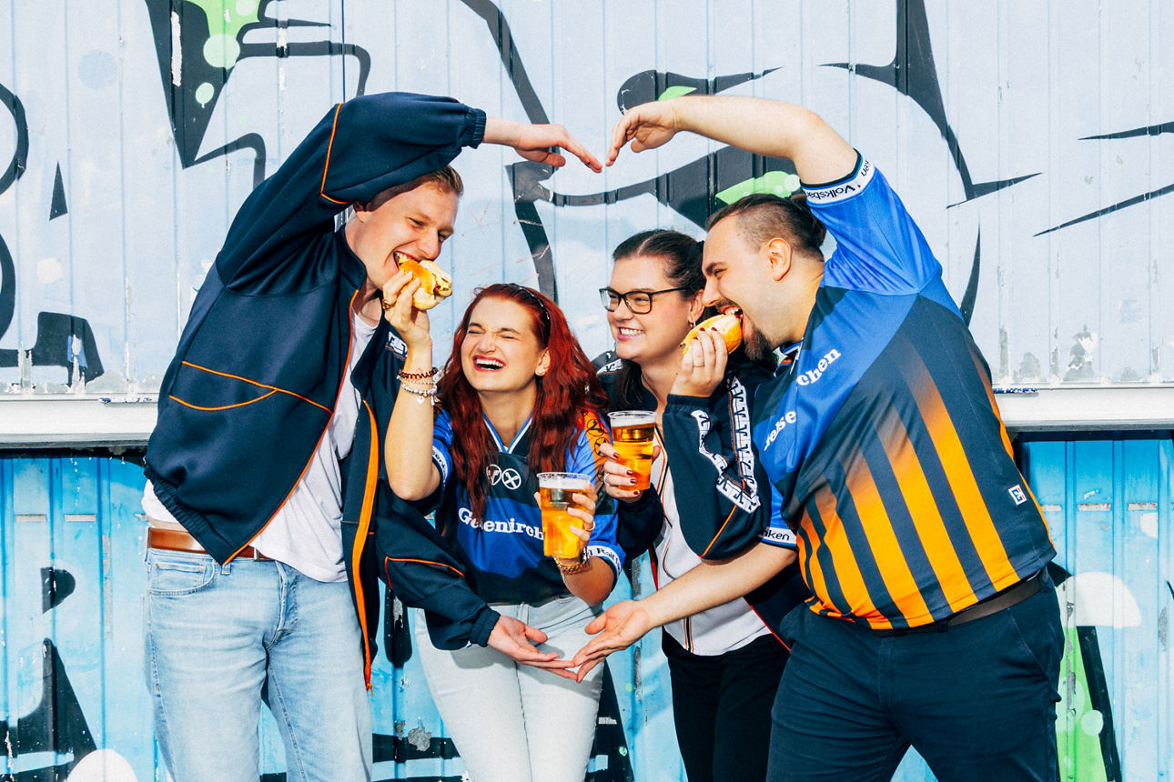 Vier junge Menschen haben Spaß vor einer Graffiti-Wand mit Bratwurst und Bier