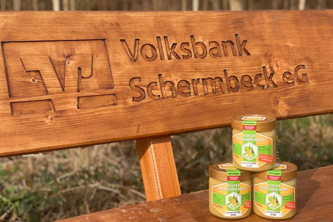 Honigglas aus dem Volksbankwald auf Holzbank mit Gravur des Logos der Volksbank Schermbeck