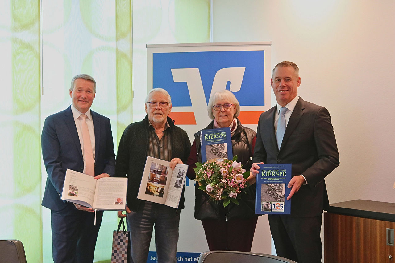 drei Männer und eine Frau stehen vor einem Volksbank Logo mit einem Buch in der Hand