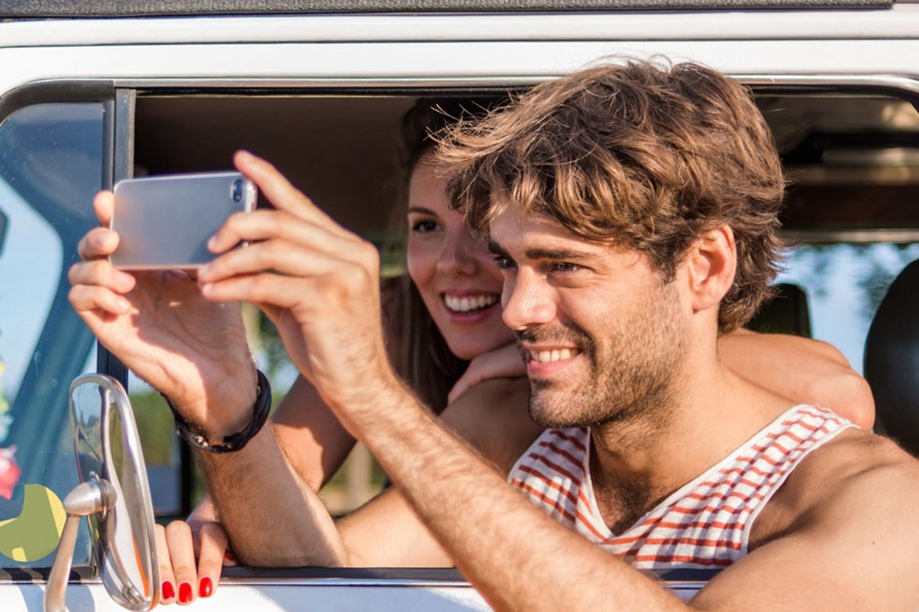 Junger Mann fotografiert mit einem Handy aus einem VW Bus