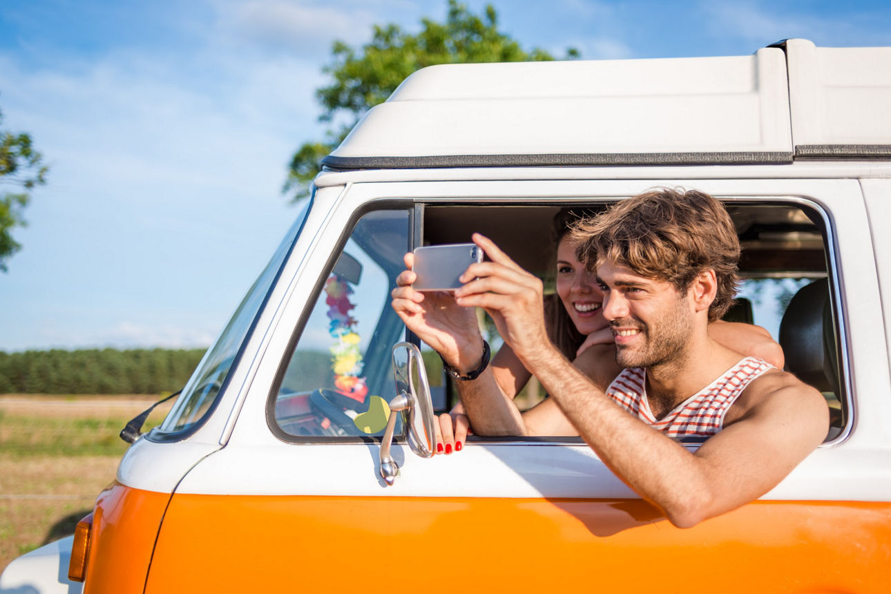 A young couple in an old camper taking pictures with smart phone