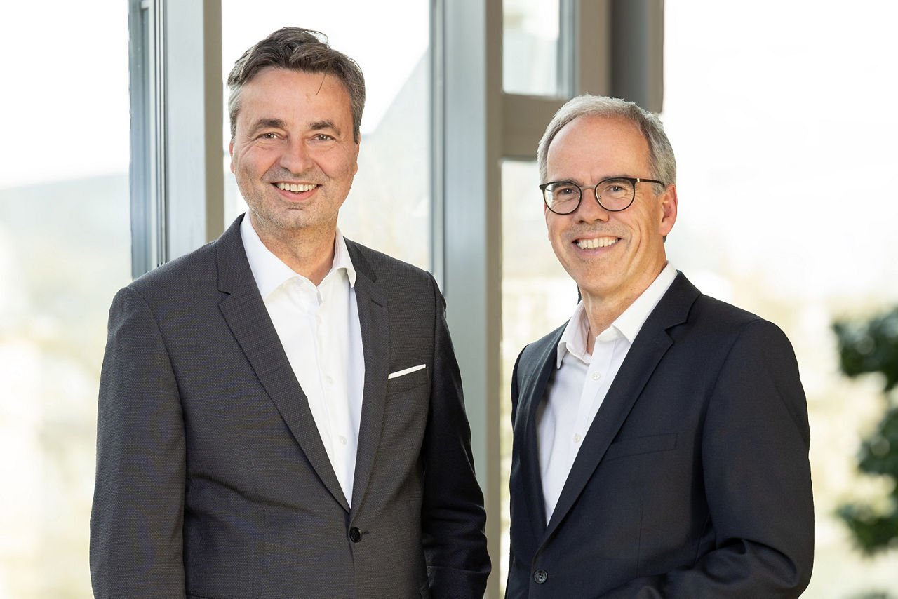 Vorstände Jörg Lott und Ingo Abrahams stehen vor einer Fensterfront