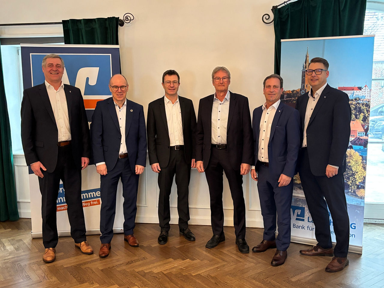 Sechs Männer in Anzüge stehen nebeneinander und lächeln in die Kamera