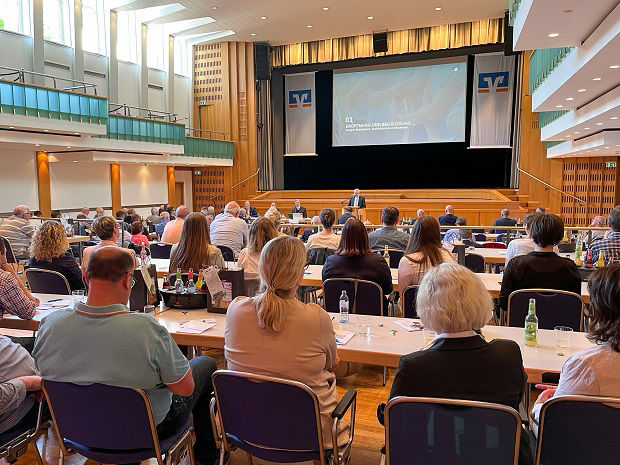 Foto unserer Vertreterversammlung. Das Foto zeigt einige Mitglieder, die sich in einem großen Saal befinden .