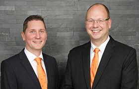 zwei Männer in Gesellschaftskleidung mit orangefarbenen Krawatten