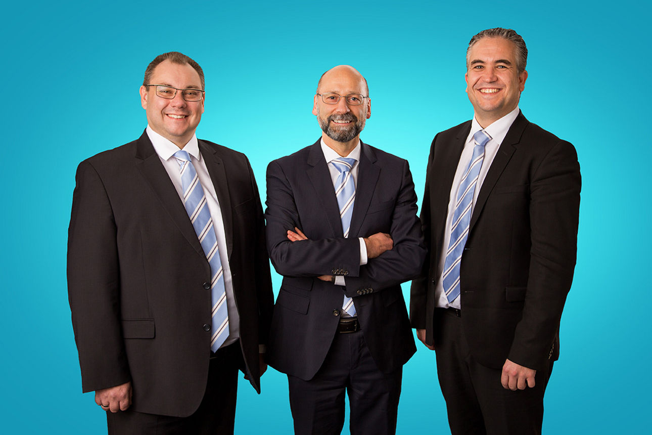 drei lächelnde Männer in schwarzen Anzügen