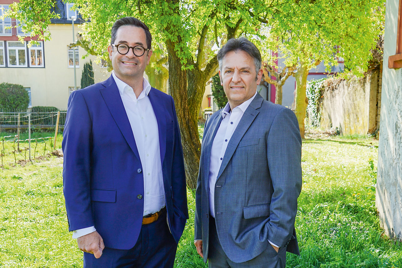 Zwei Männer stehen in Business-Kleidung im Garten auf einer Wiese