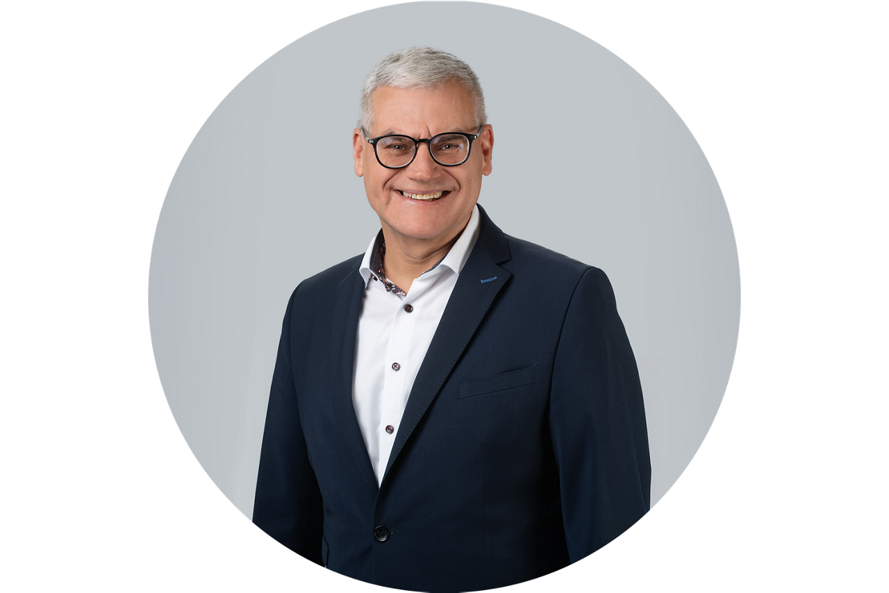 Porträt von Bruno Vey, Vorstand der VR Bank Main-Kinzig-Buedingen eG, vor grauem Hintergrund in dunklem Anzug und weißem Hemd