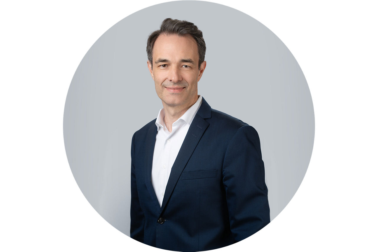 Porträt von Lars Schurich, Vorstand der VR Bank Main-Kinzig-Buedingen eG, vor grauem Hintergrund in dunklem Anzug und weißem Hemd.