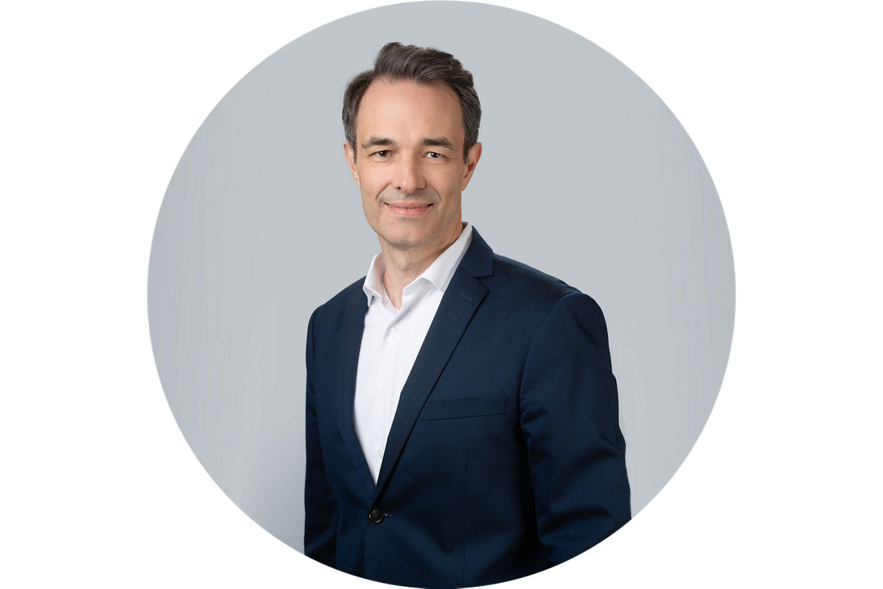 Porträt von Lars Schurich, Vorstand der VR Bank Main-Kinzig-Buedingen eG, vor grauem Hintergrund in dunklem Anzug und weißem 