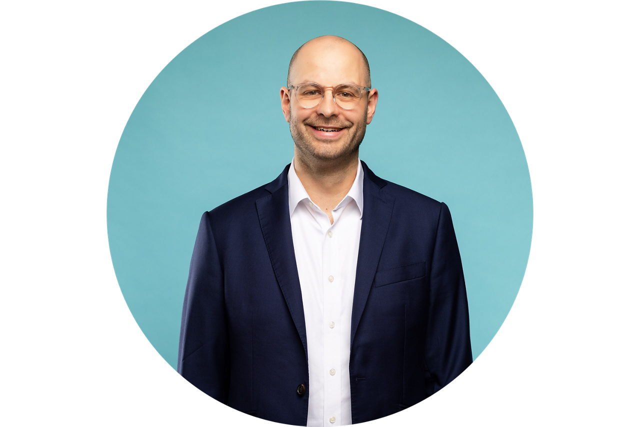 Porträt von Sebastian Emmert, Vorstand der VR Bank Fulda eG, vor hellblauem Hintergrund in dunklem Anzug und weißem Hemd.