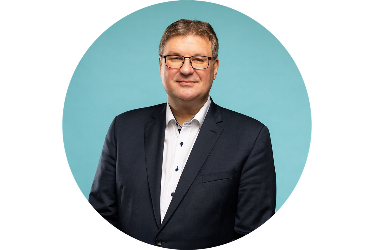 Porträt von Thomas Sälzer, Vorstand der VR Bank Fulda eG, vor hellblauem Hintergrund in dunklem Anzug und weißem Hemd.