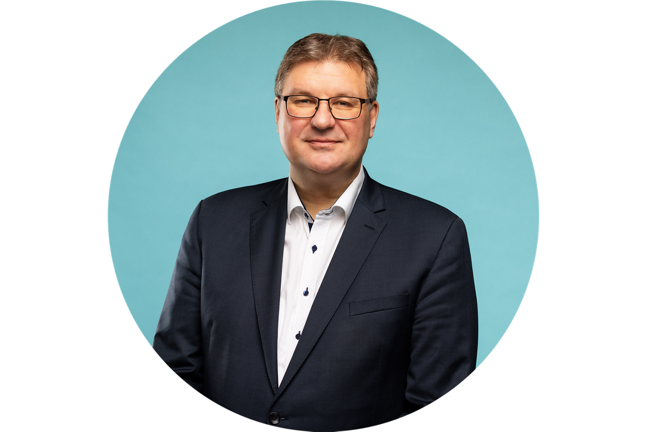 Porträt von Thomas Sälzer, Vorstand der VR Bank Fulda eG, vor hellblauem Hintergrund in dunklem Anzug und weißem Hemd.