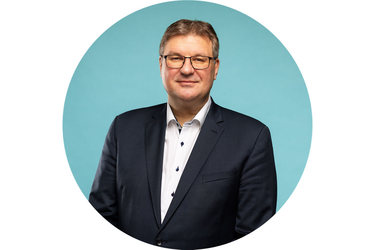 Porträt von Thomas Sälzer, Vorstand der VR Bank Fulda eG, vor hellblauem Hintergrund in dunklem Anzug und weißem Hemd.