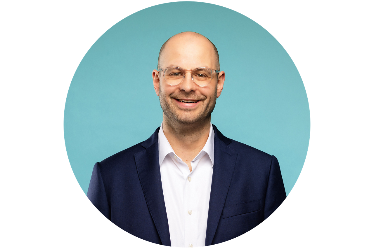 Porträt von Sebastian Emmert, Vorstand der VR RegionalBank, vor hellblauem Hintergrund in dunklem Anzug und weißem Hemd.