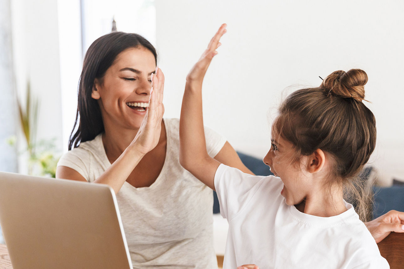 Die Mutter und die Tochter sitzen am Tisch und geben sich ein High-Five, daneben steht ein Laptop