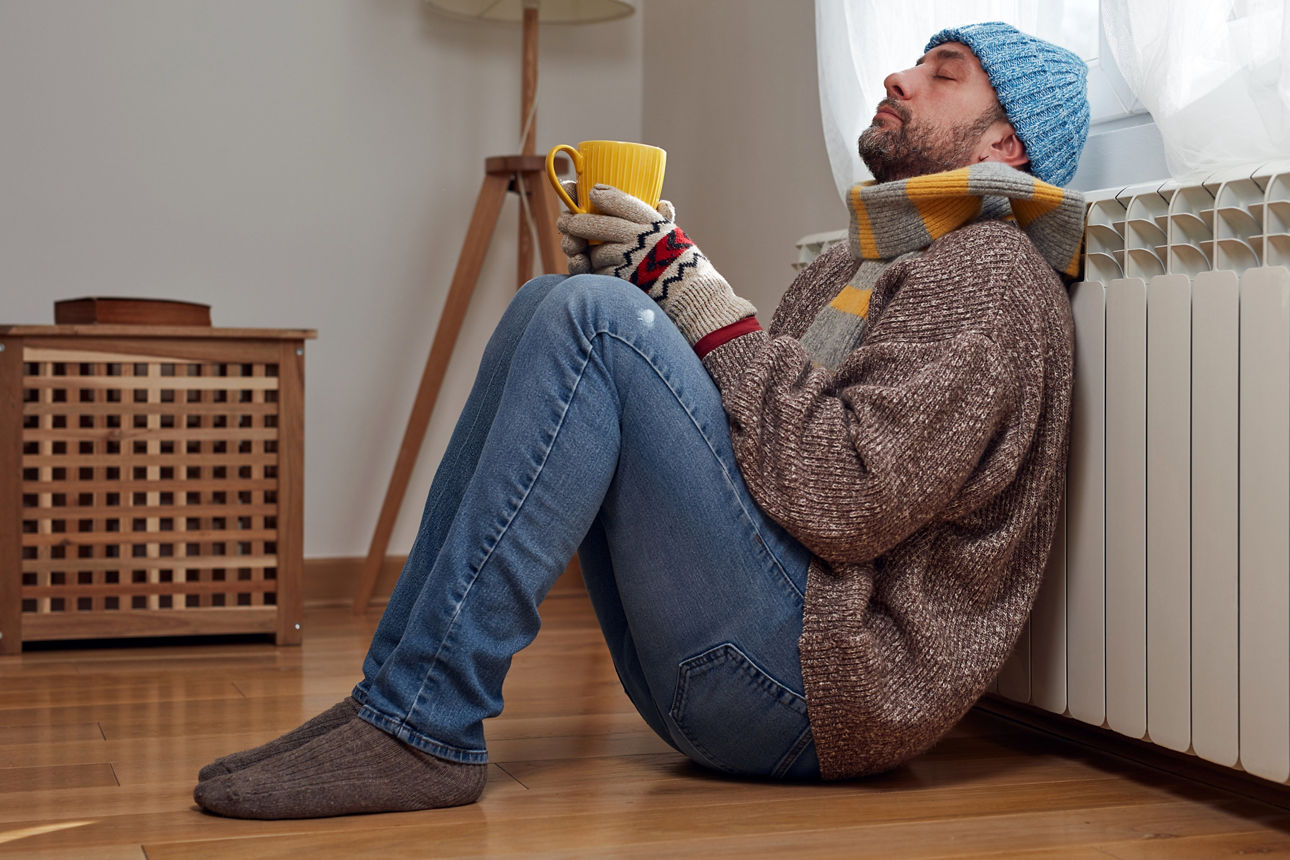 Mann in Winterklamotten lehnt an einer Heizung