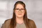 Frau mit langen braunen Haaren und Brille. Sie trägt ein beiges Top und einen Blazer.
