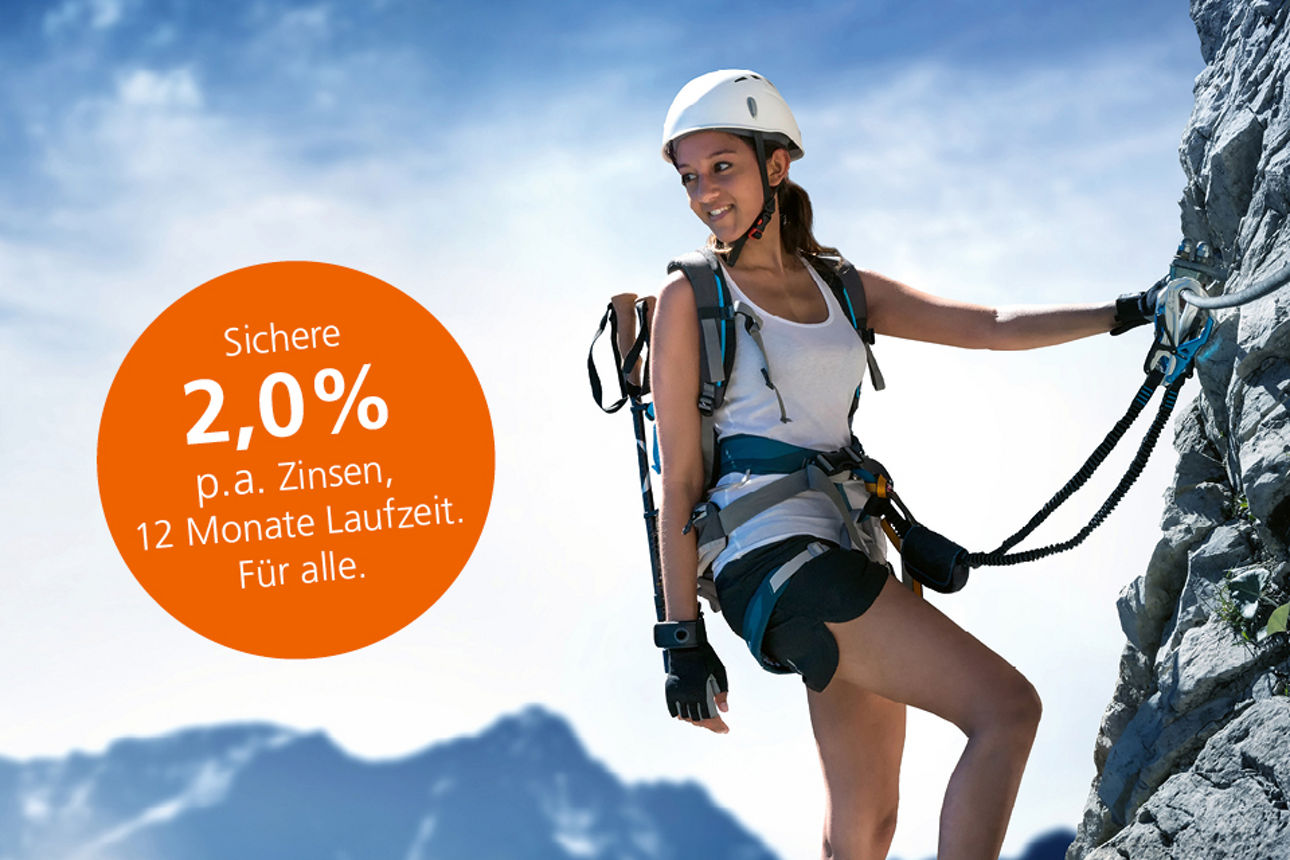 Eine junge Frau steht auf einem Klettersteig und blickt freudig in Richtung Tal