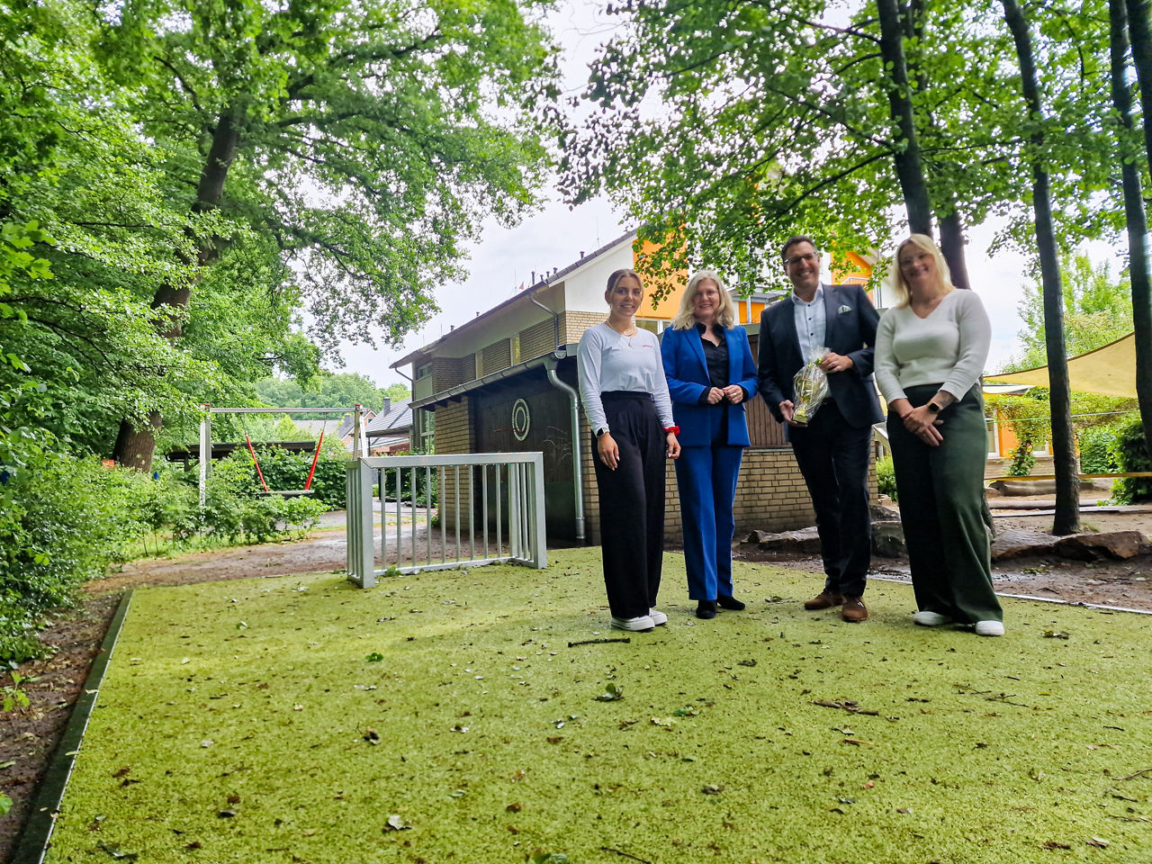 Vier Personen stehen auf dem neuen Kunstrasenplatz. Der Mann in der Mitte hält einen Pokal in der Hand.