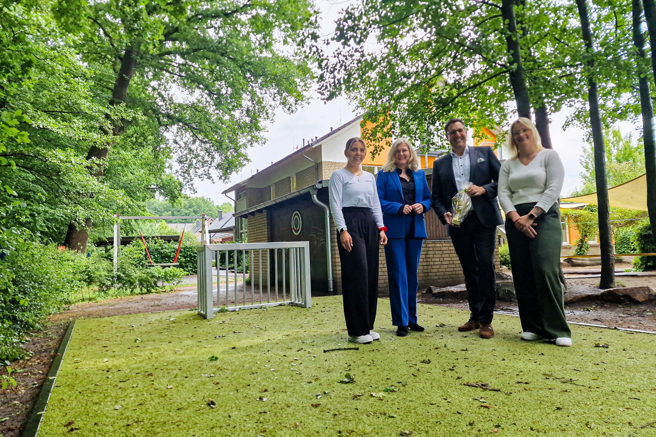 Vier Personen stehen auf dem neuen Kunstrasenplatz. Der Mann in der Mitte hält einen Pokal in der Hand.