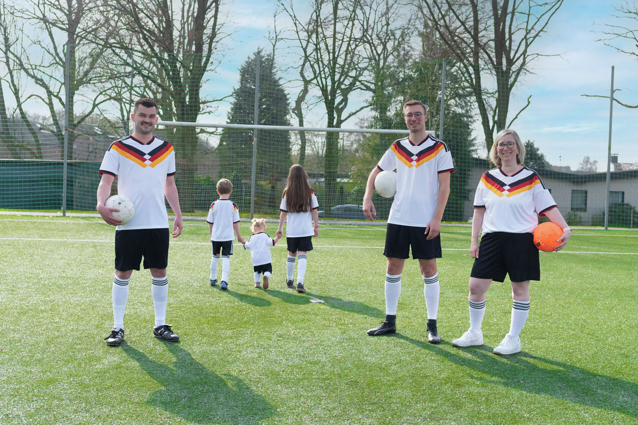 Zwei Männer, eine Frau und drei Kinder stehen in Fußballkleidung auf einem Fußballplatz
