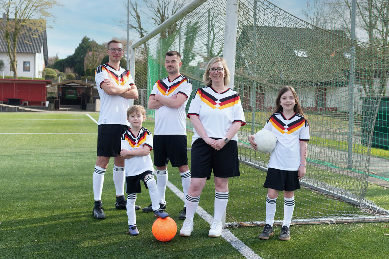 Zwei Männer, eine Frau und drei Kinder stehen in Fußballkleidung auf einem Fußballplatz