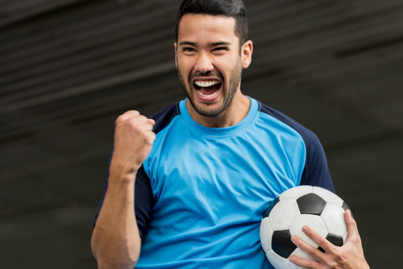 Mann mit blauem Trikot und Fussball in der Hand ballt die Faust