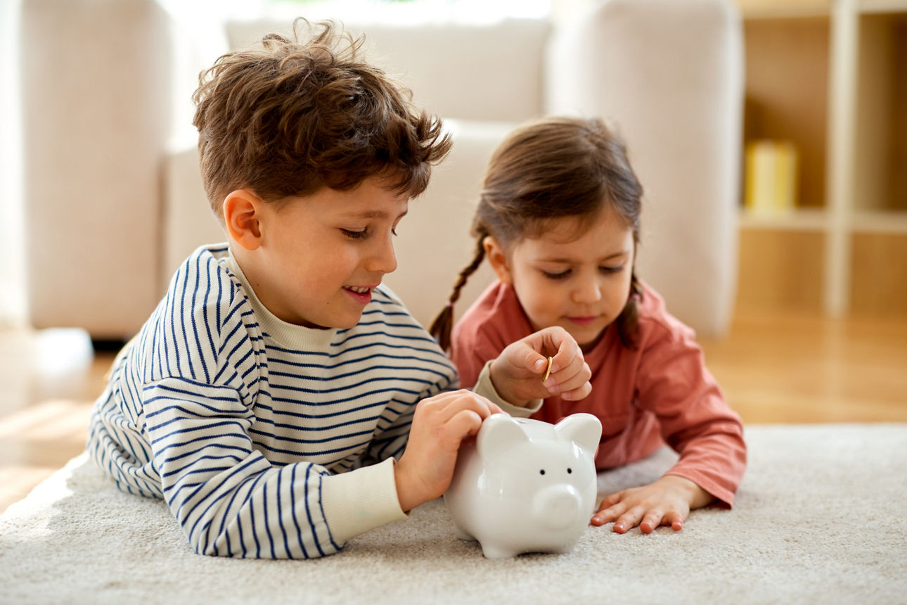 Children putting coins into piggy bank at home