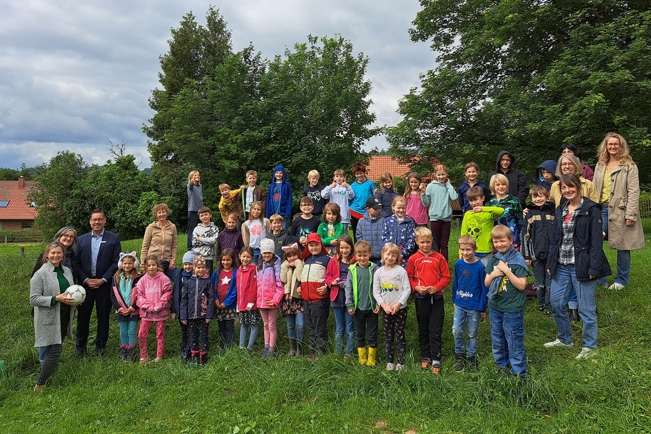 Eine Kindergartengruppe steht zusammen mit den Erziehern/innen auf der Wiese an einem Hang