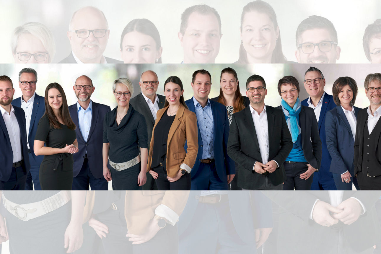 Eine Gruppe von Personen in formeller Kleidung steht zusammen vor einem neutralen Hintergrund.