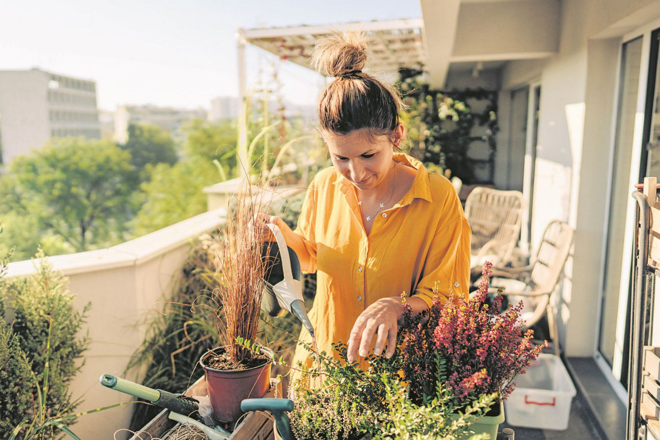 Frau giesst Blumen auf ihrem Balkon