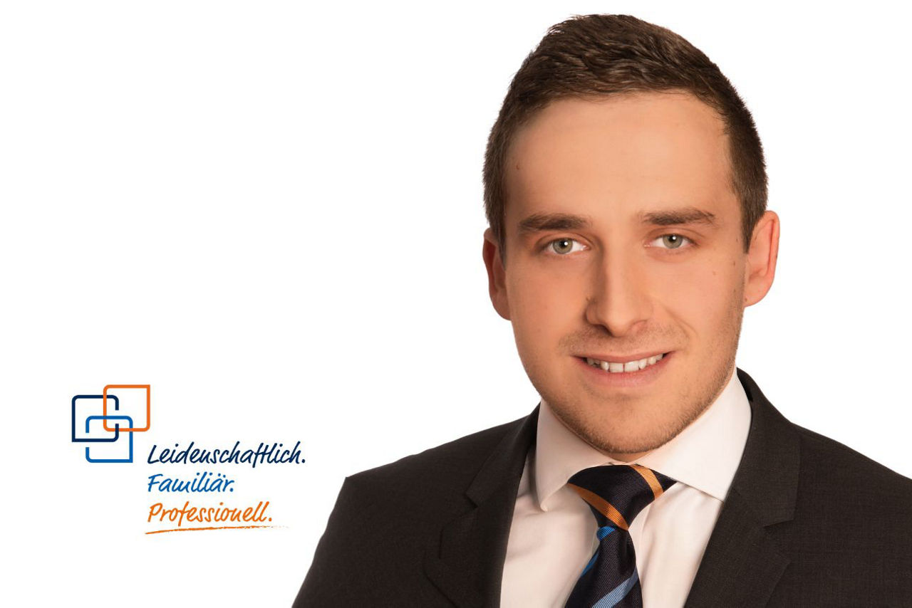 Porträt von Thomas Wagner, lächelnd, mit kurzen dunklen Haaren und einer dunkelblau-orange gestreiften Krawatte.