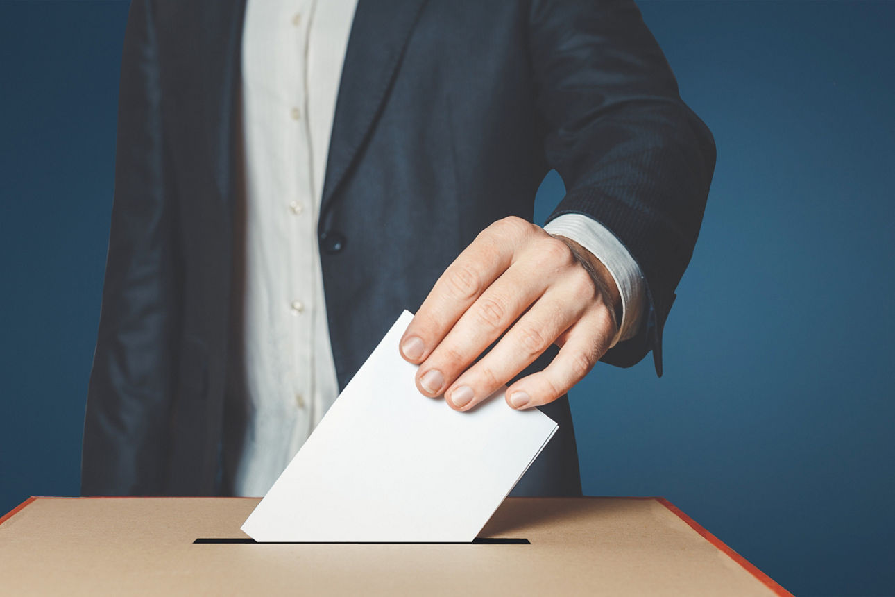 Mann steckt Wahlschein in die Wahlurne