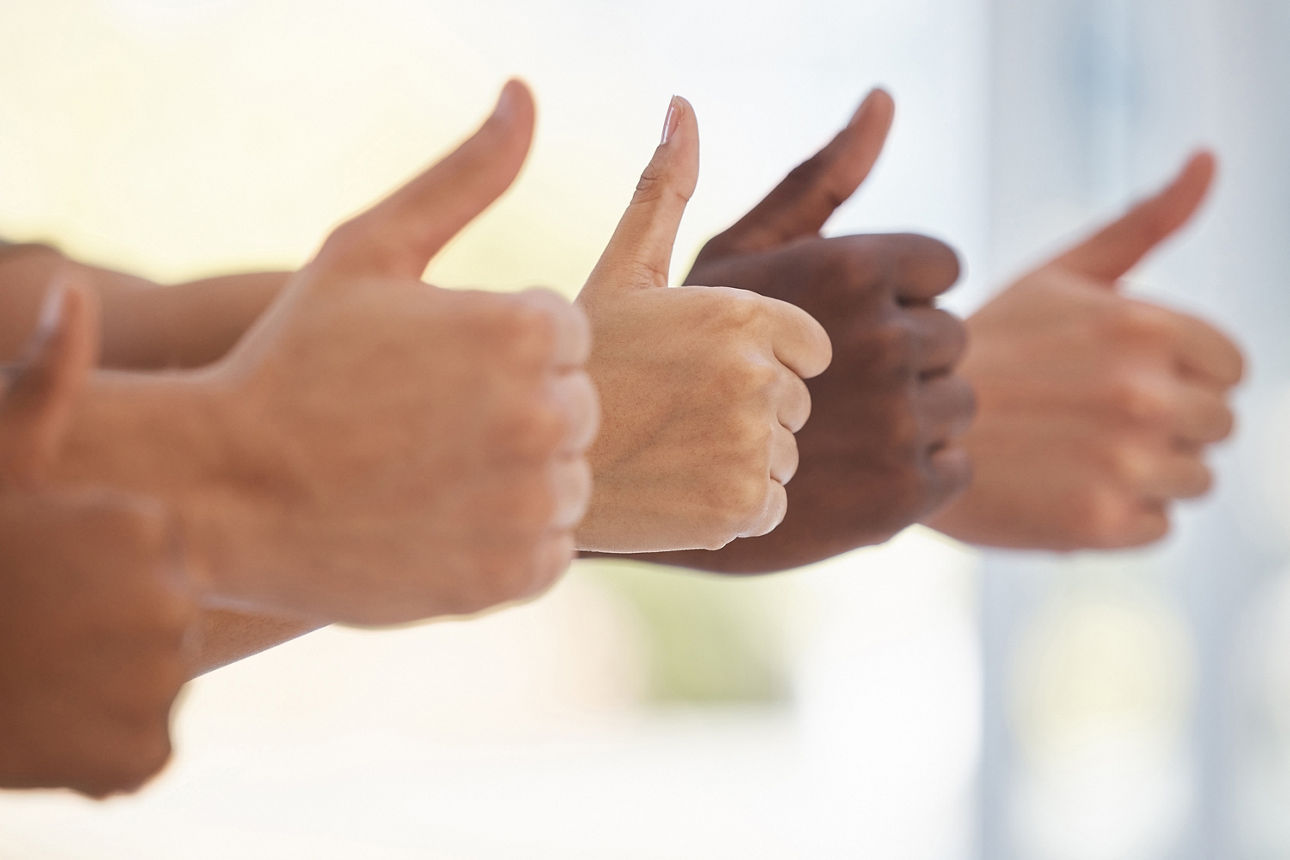 5 Hände, zustimmend mit Daumen hoch in unterschiedlichen Hautfarben. Der Hintergrund ist verschwommen. 