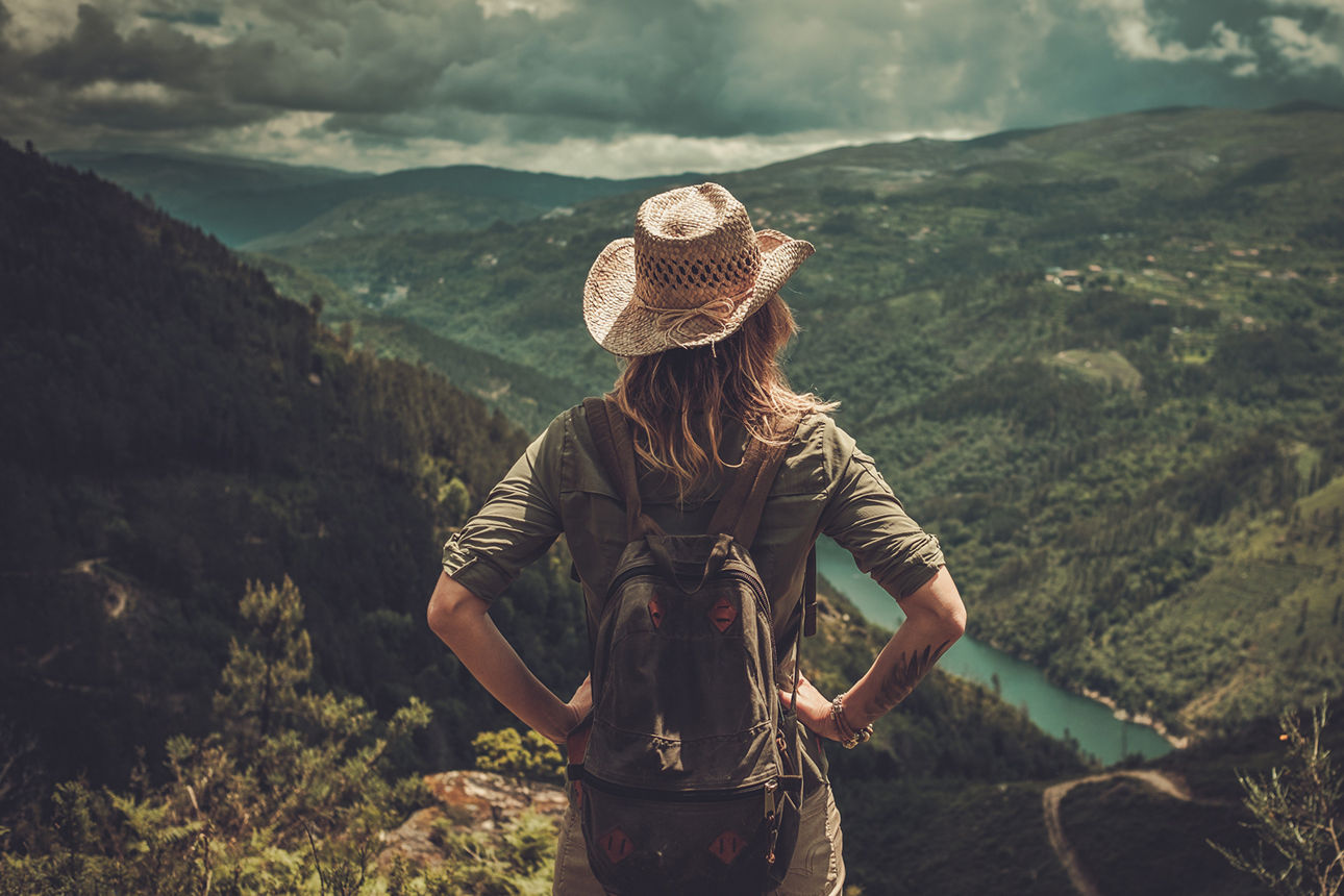 Eine Frau steht vor einer Schlucht, in der viele Bäume wachsen. Sie trägt Wanderkleidung.