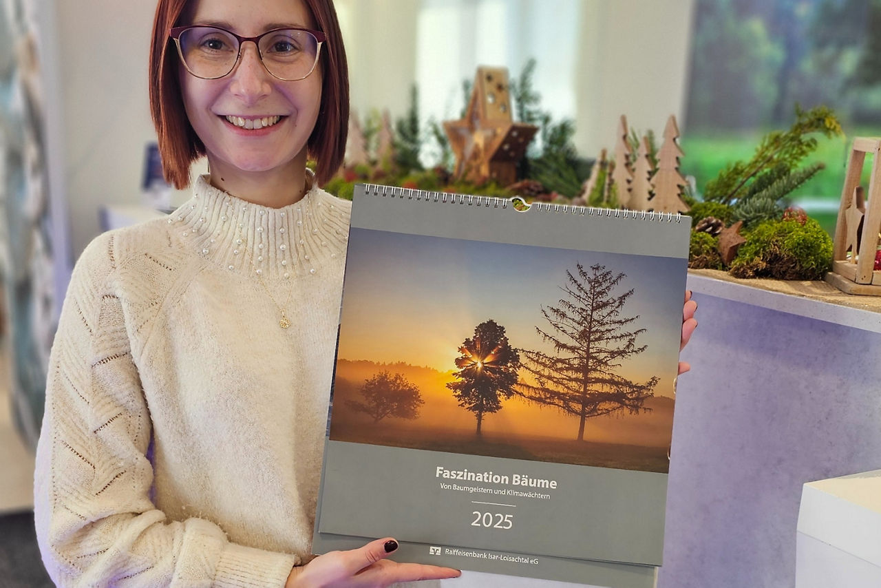 Mitarbeiterin hält Bild-Kalender 2025 hoch