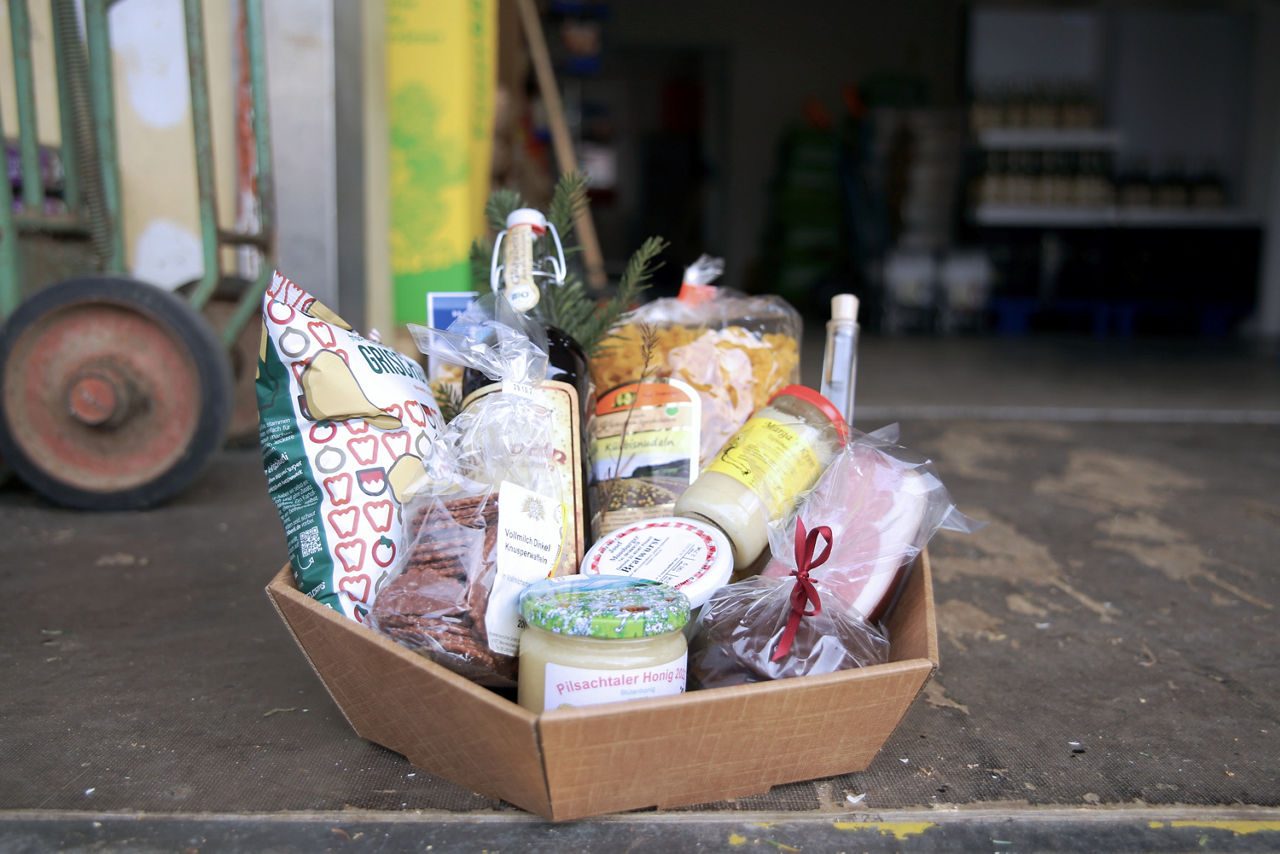 Geschenkkorb mit diversen Lebensmitteln wie Honig, Glühwein, Nudeln und Speck