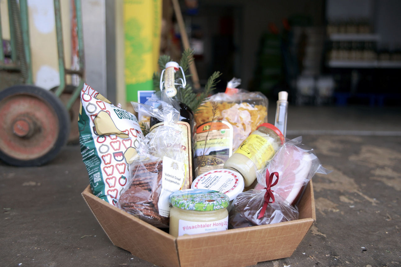 Geschenkkorb mit diversen Lebensmitteln wie Honig, Glühwein, Nudeln und Speck