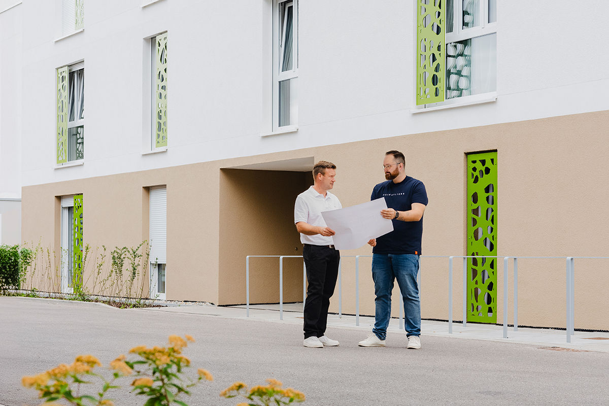 Zwei Männer gehen an einem Industriegebäude vorbei und unterhalten sich